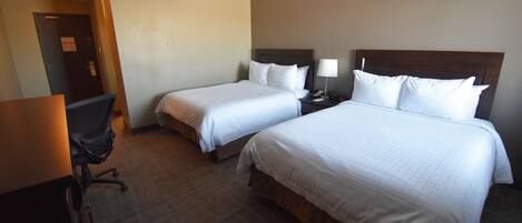 A hotel room with two single beds, a desk, and a chair.