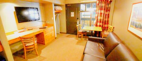 A compact living space with a sofa, a dining table, a TV, and a kitchenette.