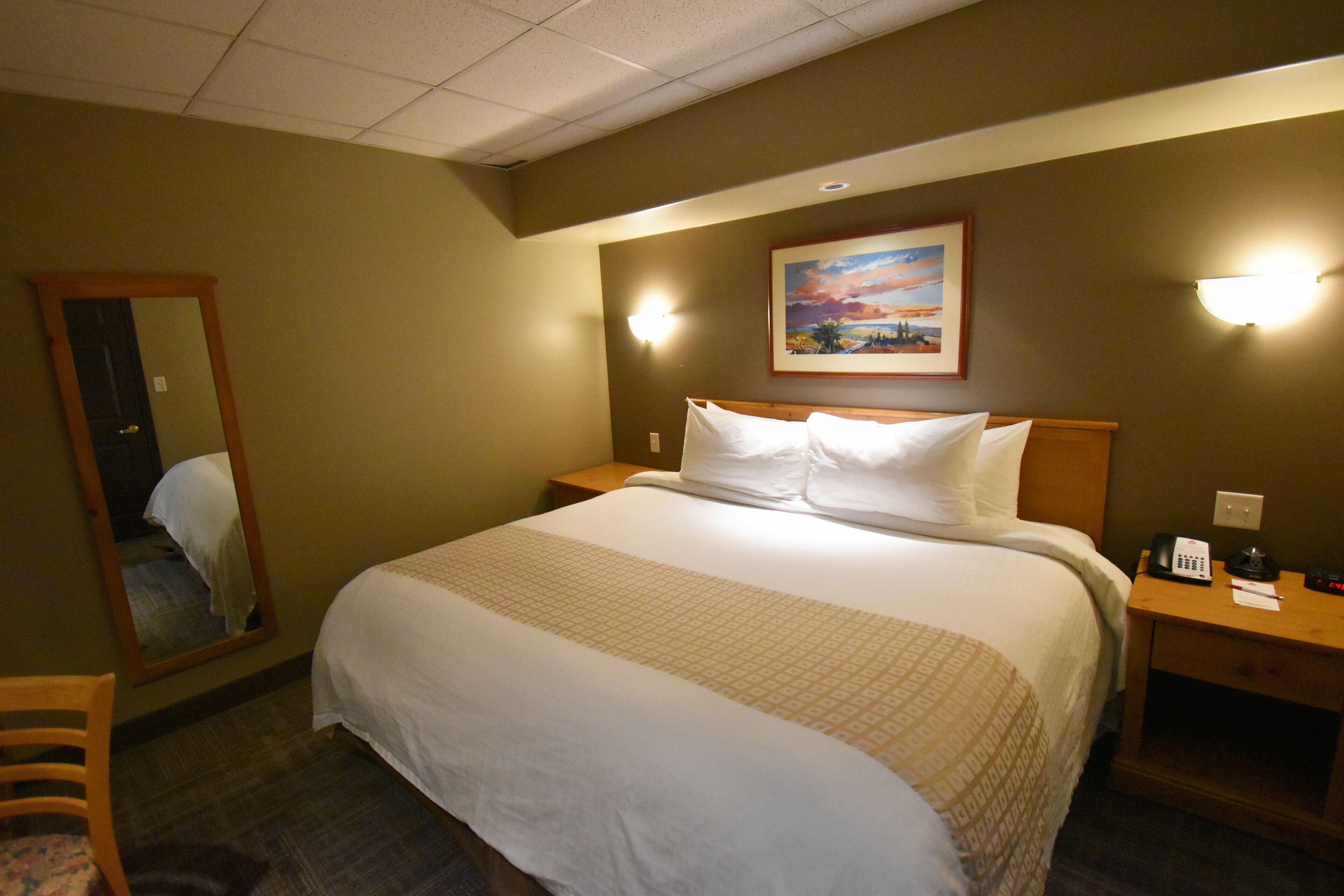 A hotel room with a large bed, a nightstand, a mirror, and a painting on the wall.