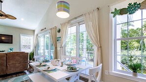 Un comedor con una mesa blanca para cuatro personas, ventanas amplias con cortinas, un ventilador de techo y vistas al exterior.