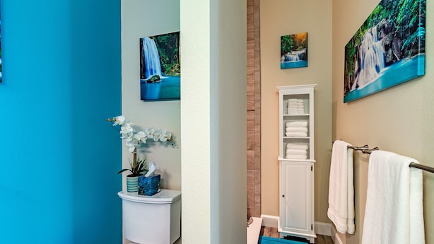Une salle de bain avec des toilettes, un lavabo et un espace de douche bleu. Des serviettes sont suspendues sur un porte-serviettes et une petite étagère contient des articles de toilette.