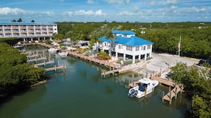 Un puerto deportivo con barcos amarrados, un edificio blanco con techos azules y un gran hotel al fondo.