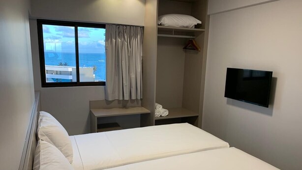 A hotel room with a bed, a TV, a window with a view of the sea, and a closet with a hanging rack. - Excelentes Duplex Maceió (Maceió)