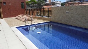 A swimming pool with a tiled edge, a metal ladder, and a brick wall. - Excelentes Duplex Maceió (Maceió)