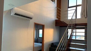 A compact room with a desk, chairs, a bed, a staircase, and a large window. - Excelentes Duplex Maceió (Maceió)
