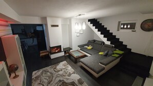 Una sala de estar moderna con un sofá, una chimenea, una escalera y lámparas colgantes.