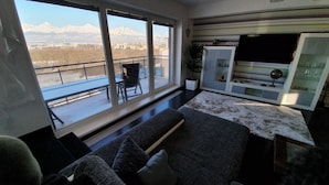 Una sala de estar moderna con un ventanal grande, un sofá, un mueble para TV y vistas a montañas.