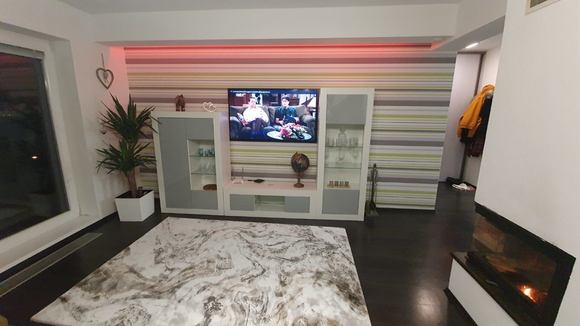 A modern living room with a flat-screen TV, a marble rug, and a striped wall.