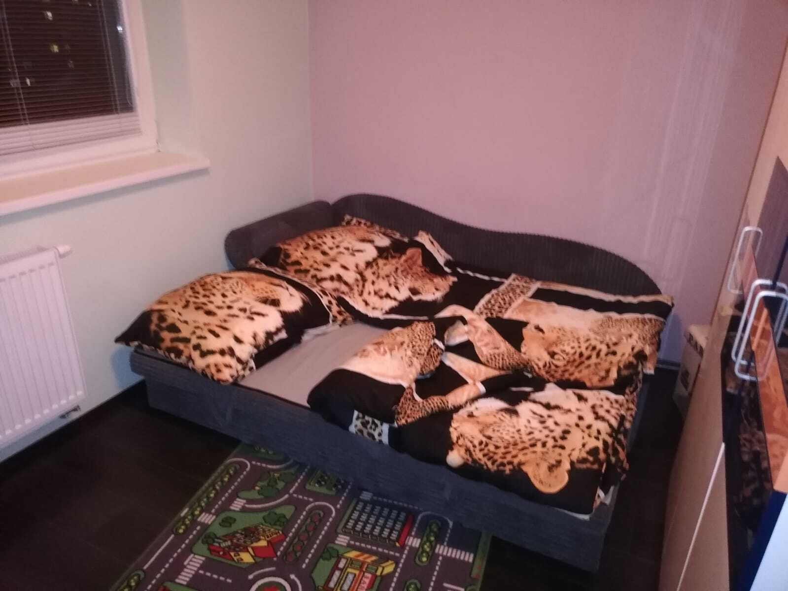 A bedroom with a bed covered in leopard print bedding, a window with blinds, and a radiator.