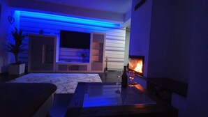 Una sala de estar moderna con chimenea, un ventanal grande y una luz ambiental azul.