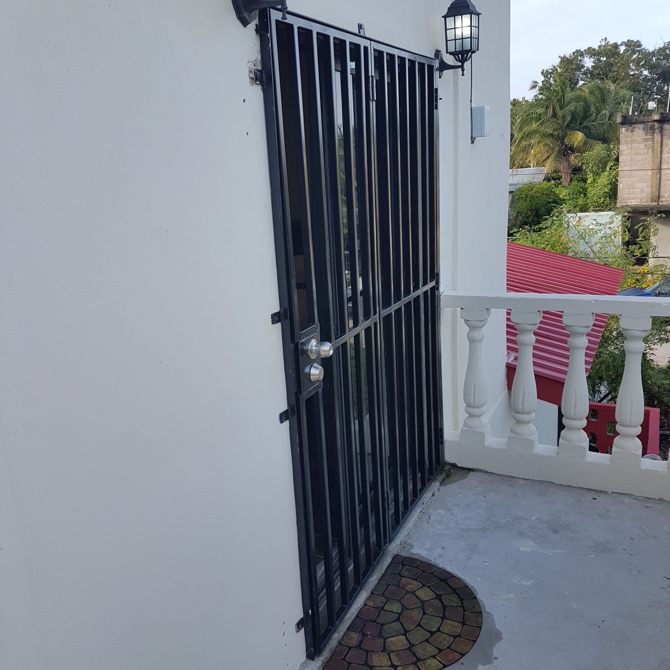 A gated balcony with a white railing and a red roof visible in the background.