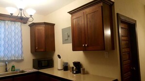 Een keuken met houten kastjes, een magnetron, een koffiezetapparaat en een raam met gordijnen met een patroon.