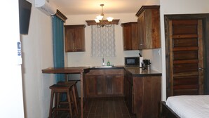 Een kleine keuken met houten kastjes, een ingebouwde magnetron en een barretje met krukken.
