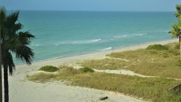A beach with clear blue water, sandy shore, and sparse vegetation. - Beachcomber unit 507 (Longboat Key)
