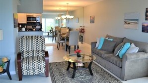 A living room with a sofa, armchair, and coffee table. There is a dining area with chairs and a table in the background. - Beachcomber unit 507 (Longboat Key)