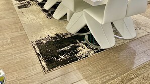 Uma sala de jantar moderna com uma mesa comprida posta para refeição, cadeiras brancas e uma tela de televisão ao fundo.