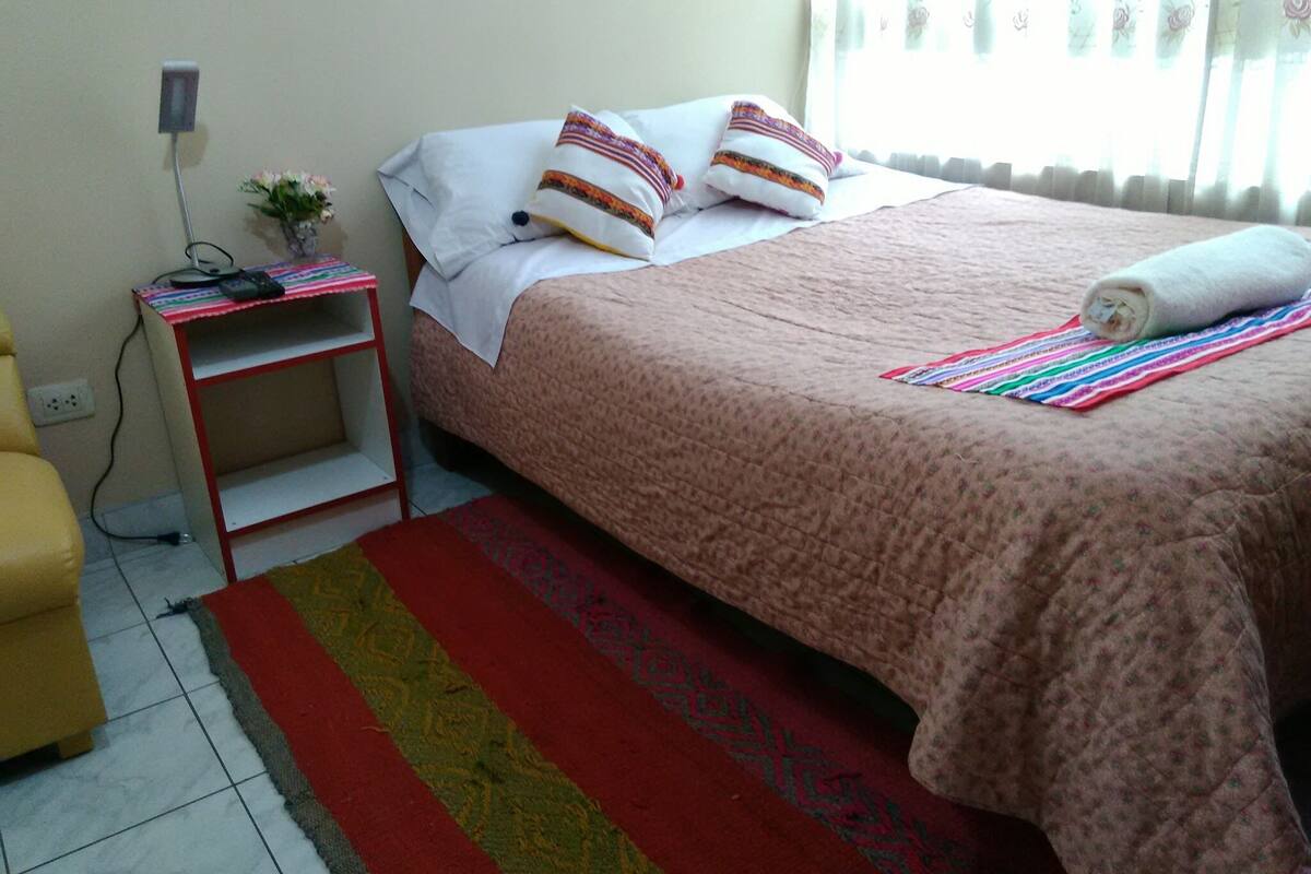 A bedroom with a bed, a nightstand, a chair, and a window with curtains.