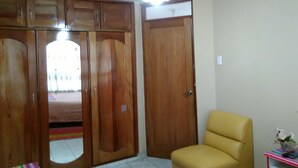 A room with a wooden wardrobe, a yellow chair, and a small table with a vase. - Shanell House - Hostel (Cusco)