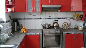 A kitchen with red cabinets, a gas stove, a kettle, and a sink. - Shanell House - Hostel (Cusco)