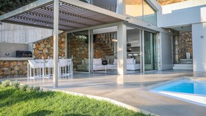 Una casa moderna con un porche cubierto, piscina y un muro de piedra.