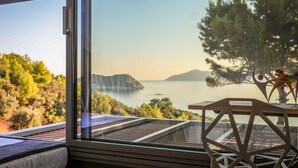 Una habitación con un amplio ventanal que ofrece una vista panorámica del agua, árboles y una montaña distante.