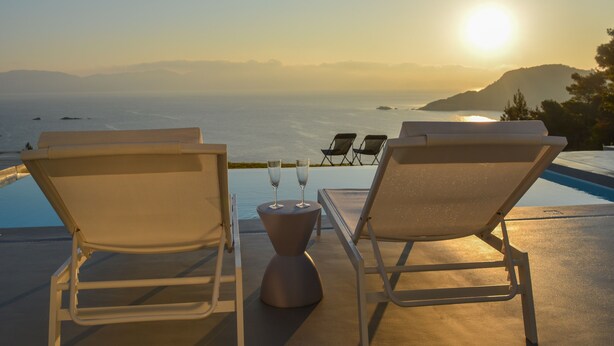 Deux fauteuils confortables placés face à une piscine, offrant une vue sur le coucher de soleil et l’océan.