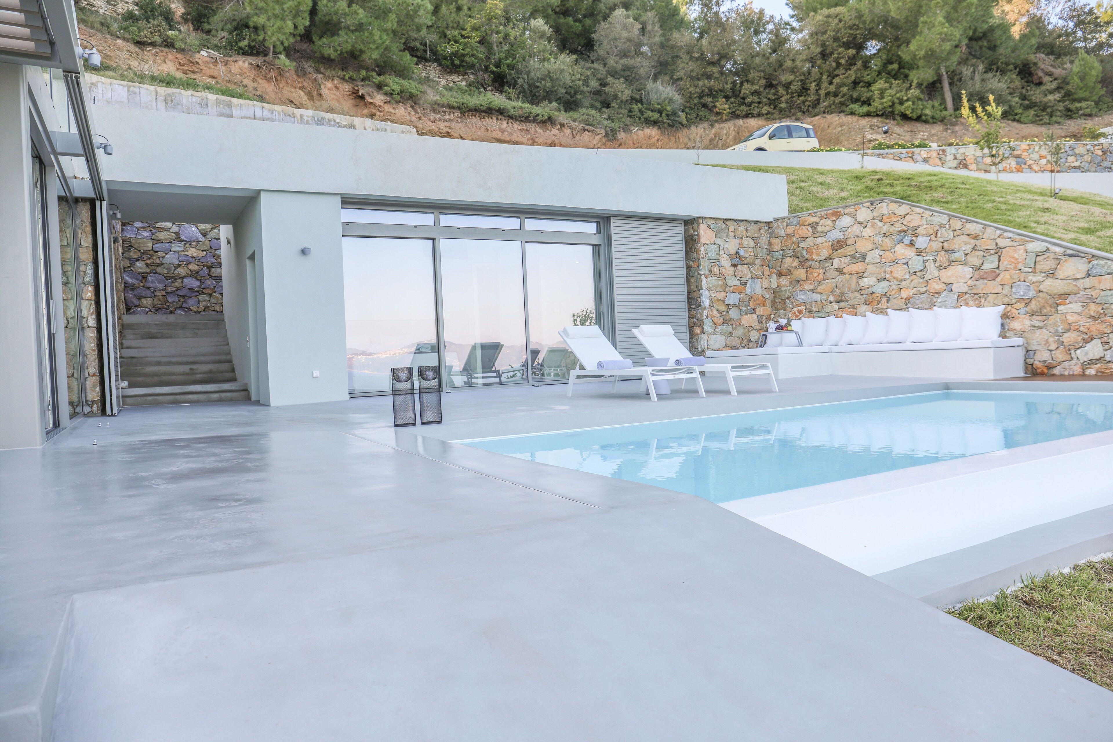 Un espace piscine moderne agrémenté d’un mur en pierre, d’un canapé d’extérieur blanc et de chaises longues.