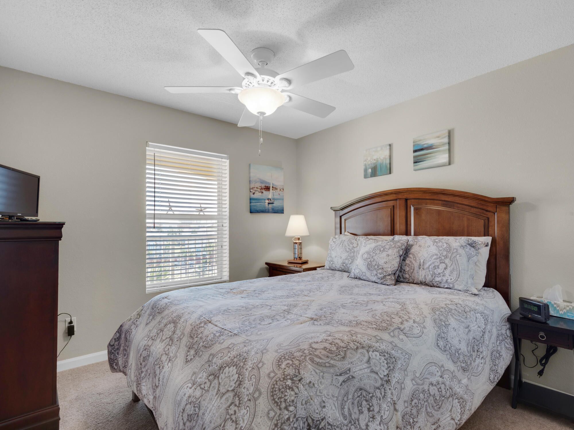 A bedroom with a bed, a ceiling fan, a nightstand, a lamp, and a TV.