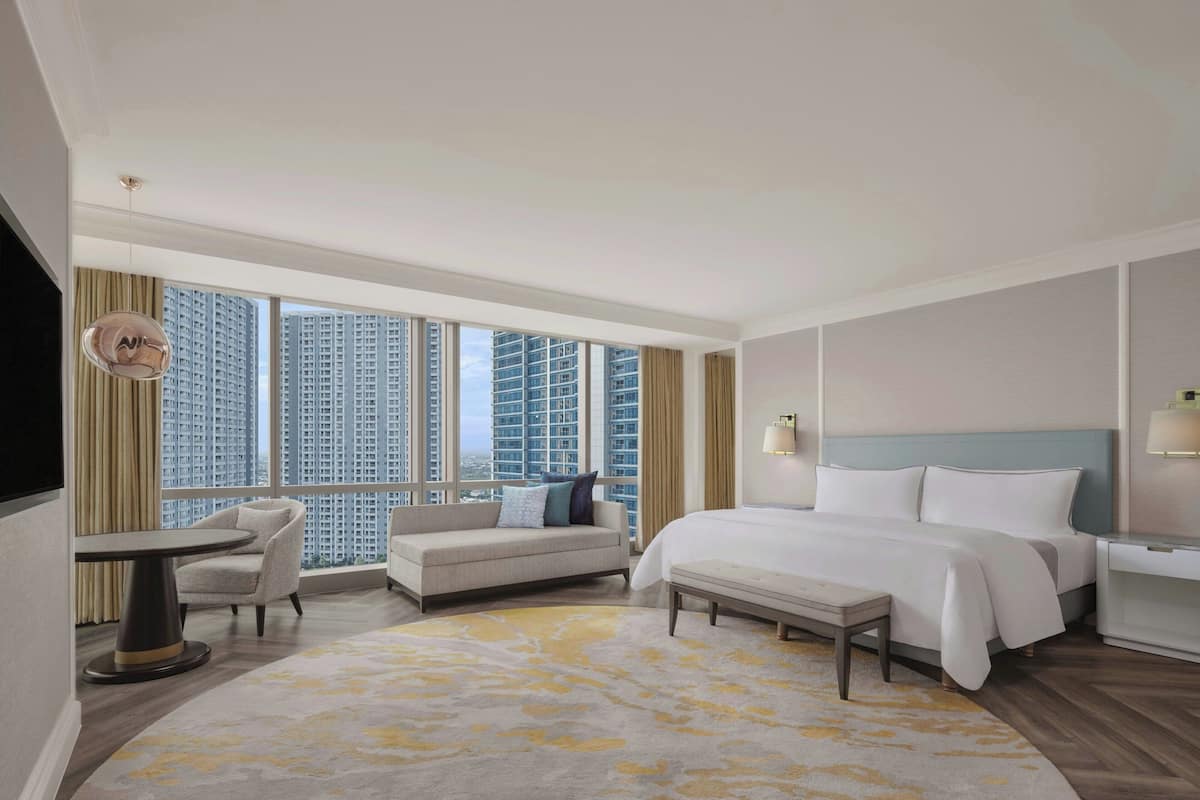 Habitación de hotel con una cama grande, un sofá, una mesita y vistas a edificios altos.