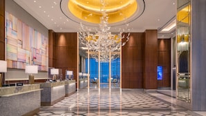 Een ruime lobby met een moderne kroonluchter, een receptiebalie en een groot abstract schilderij aan de muur.