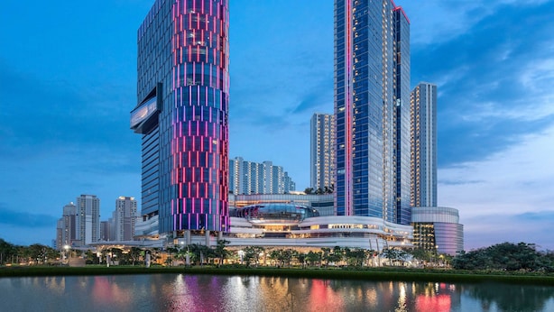 Een modern hotel met een opvallende roze en blauwe gevel, omringd door hoge gebouwen en een waterpartij.