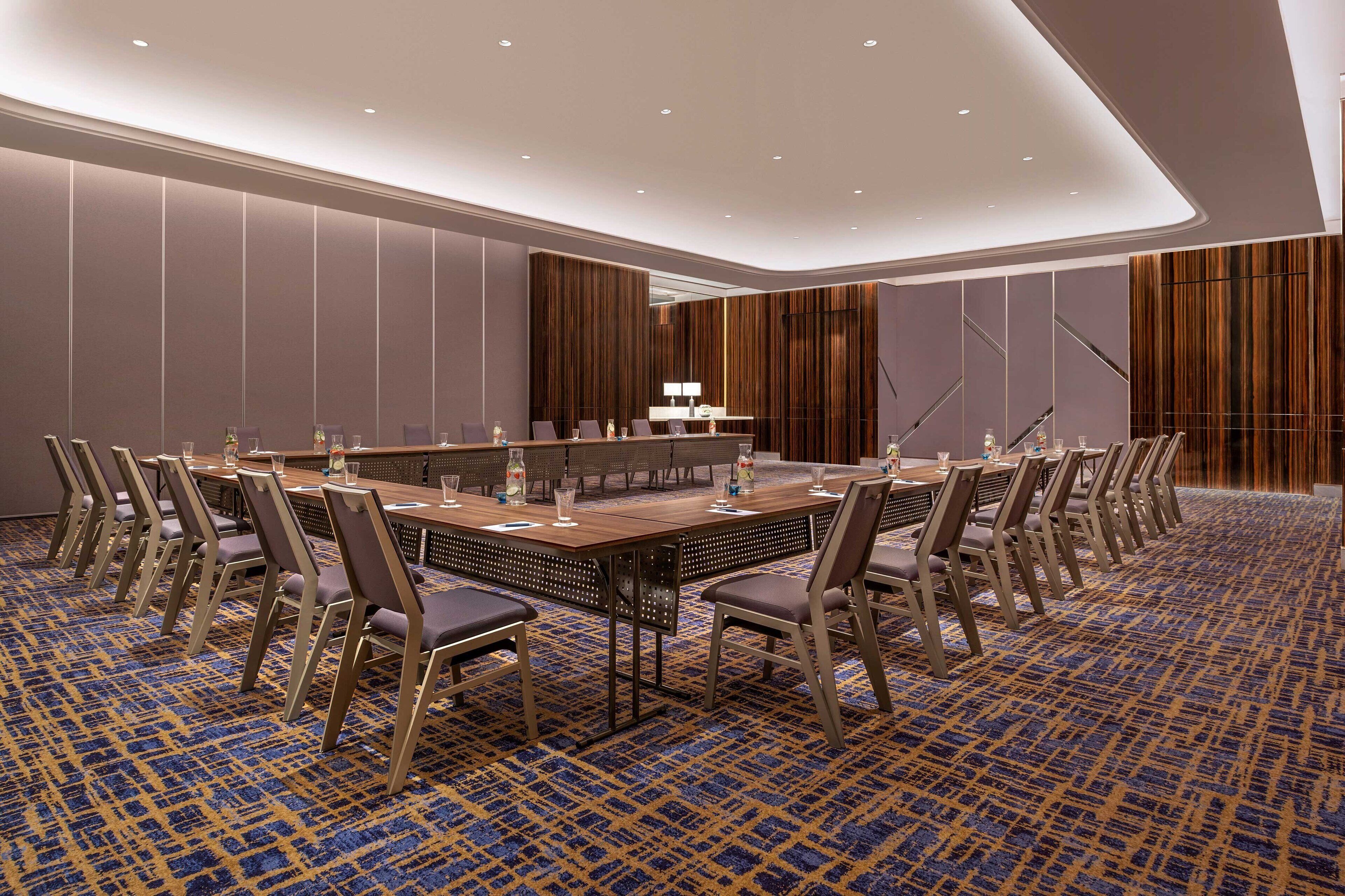 Un salón de conferencias con una larga mesa, sillas y un pequeño escenario.