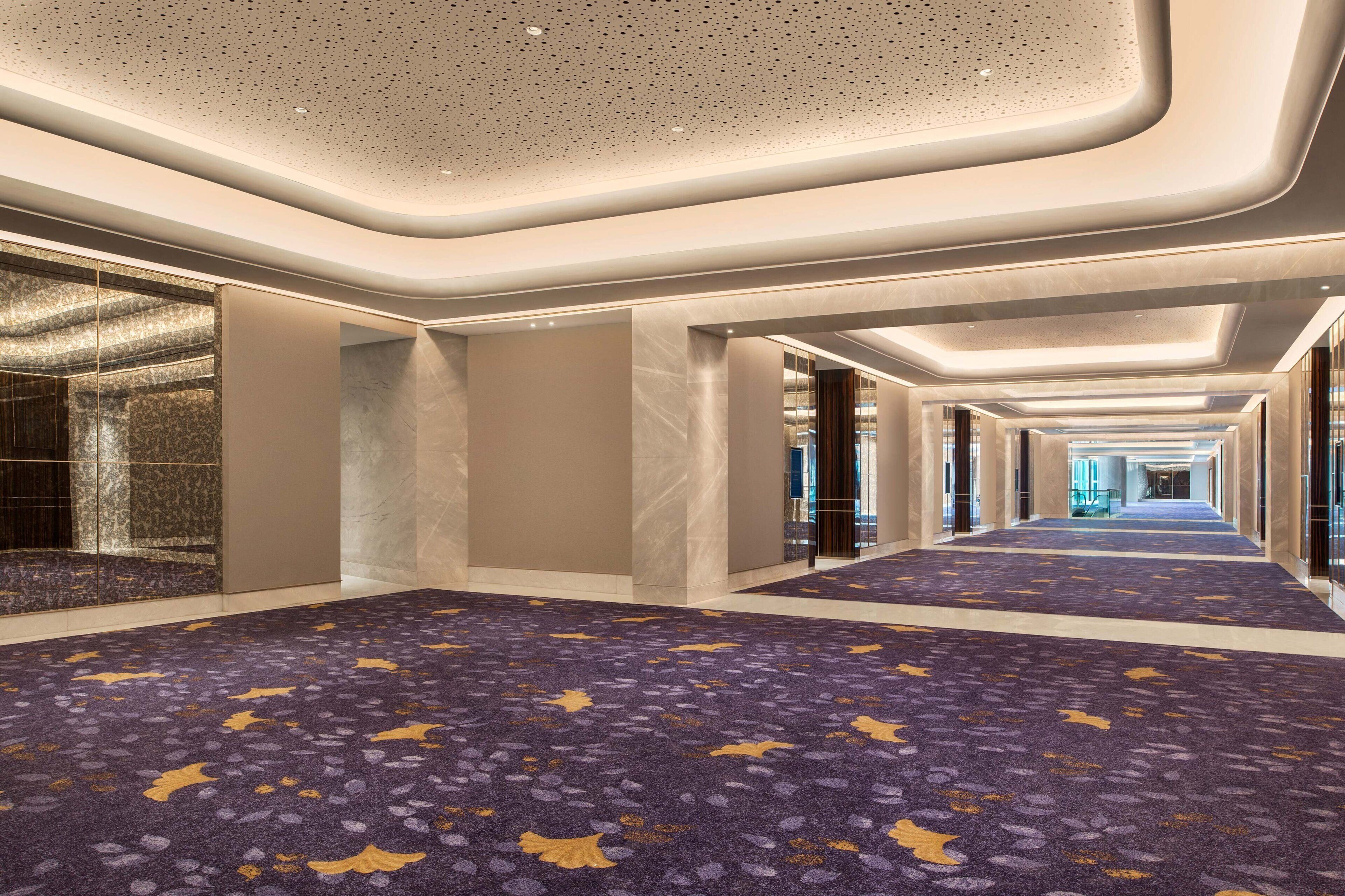 A long, well-lit corridor with a patterned carpet, marble walls, and a modern ceiling design.