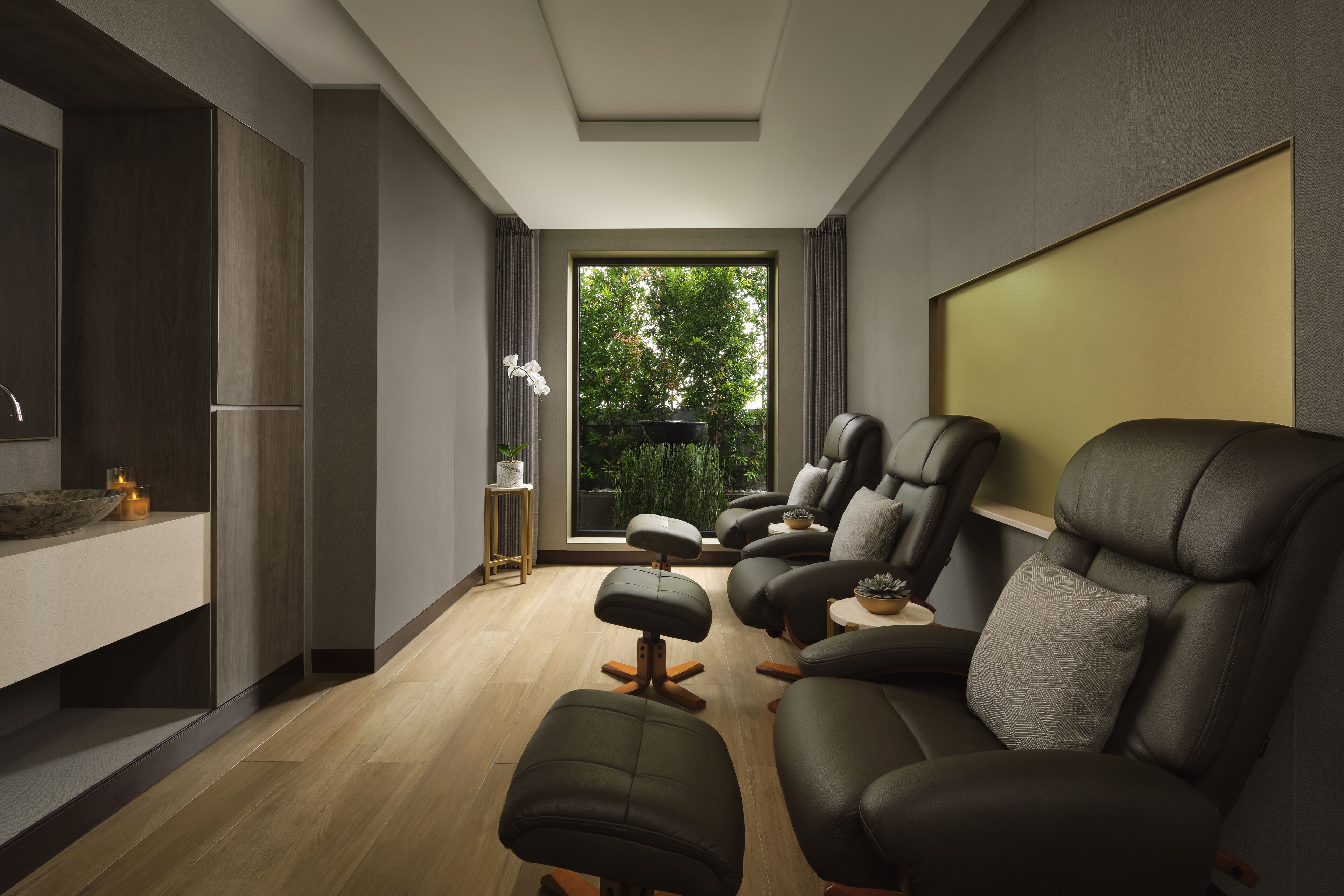 Una sala de estar moderna con un sofá, un reposapiés y un ventanal con vistas a zonas verdes.