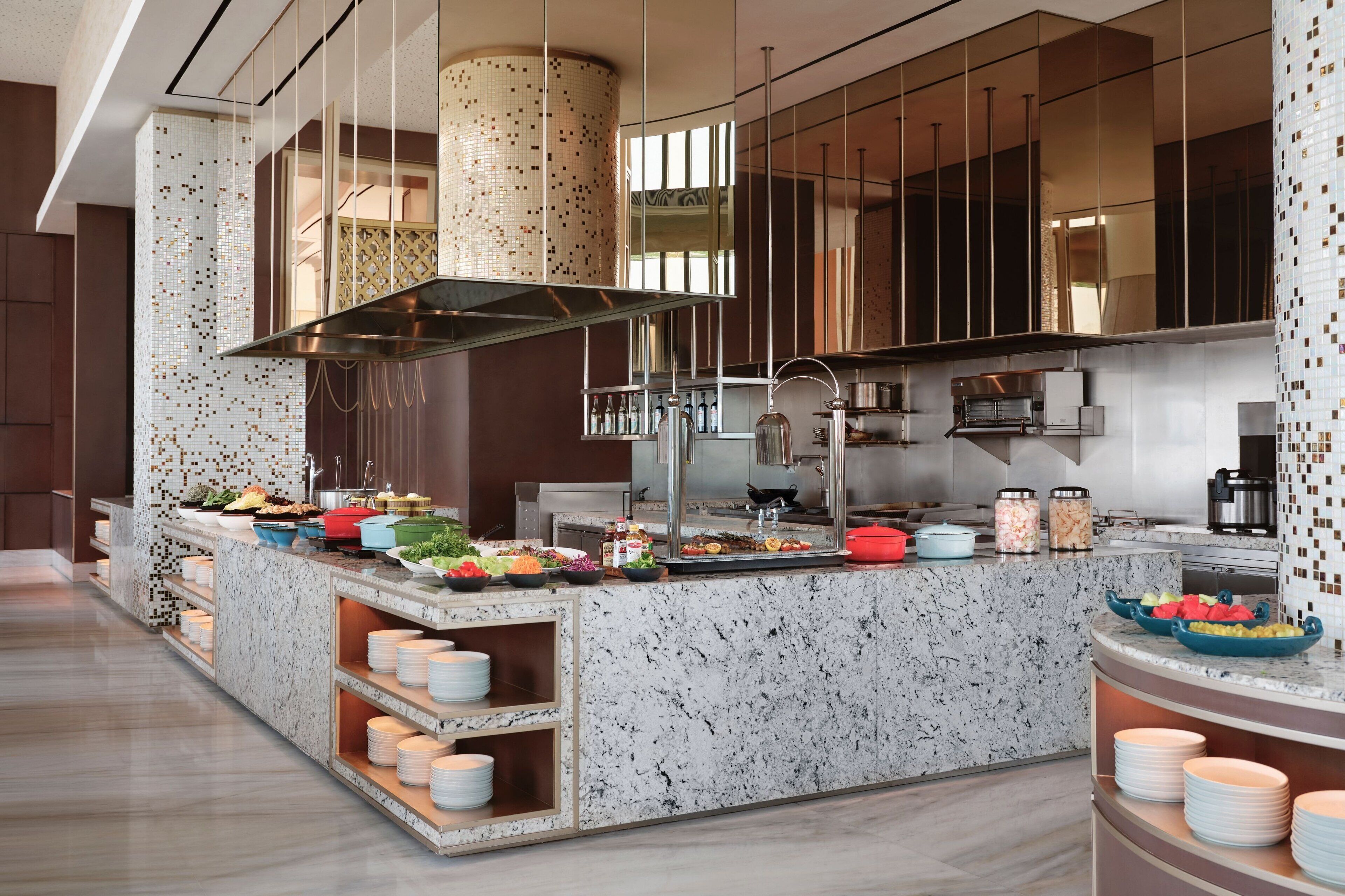 A modern kitchen with a marble countertop, stainless steel appliances, and a variety of food items displayed.