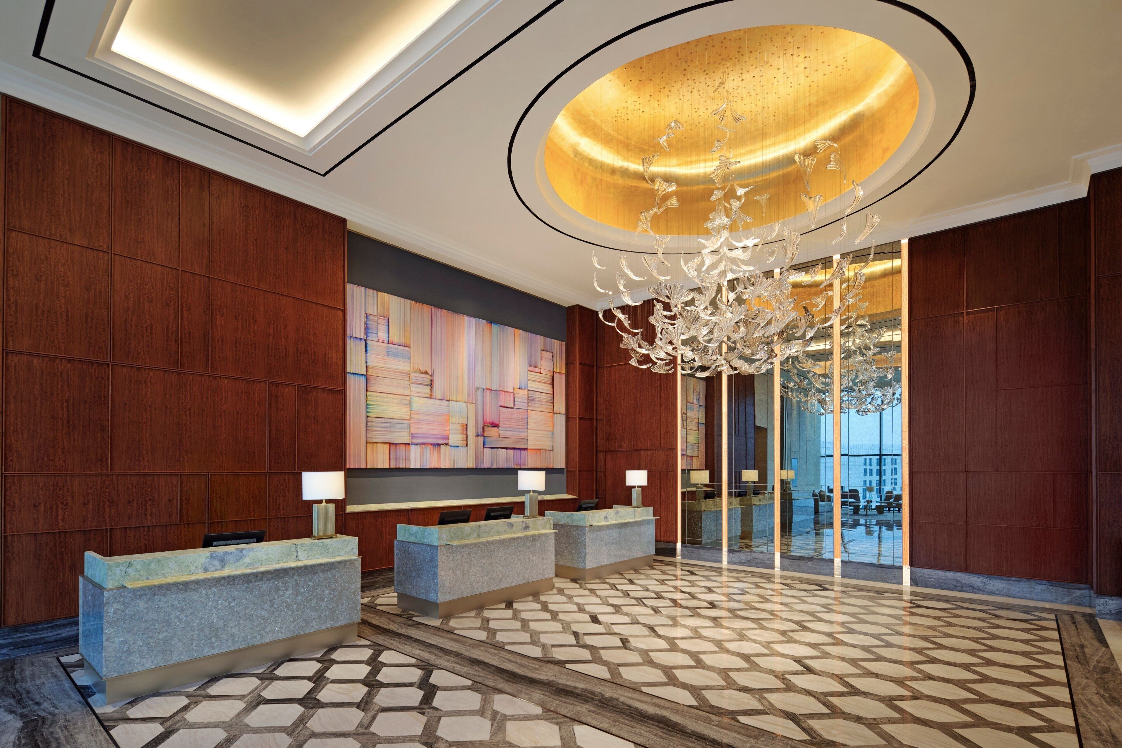 A lobby with a reception desk, a chandelier, and a large abstract painting on the wall.