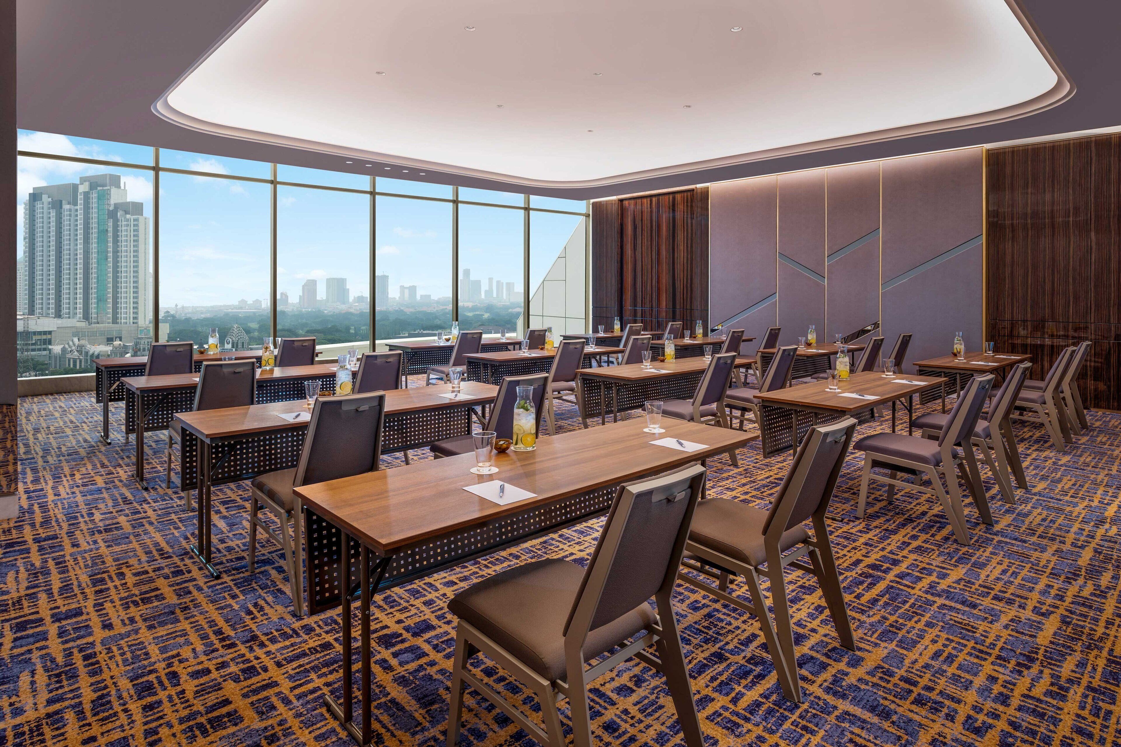 A conference room with multiple tables and chairs, large windows offering a city view, and a patterned carpet.