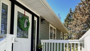 Une maison avec une porte d’entrée blanche, un paillasson noir, une clôture en bois peinte en blanc et un pot de fleurs sur le porche.