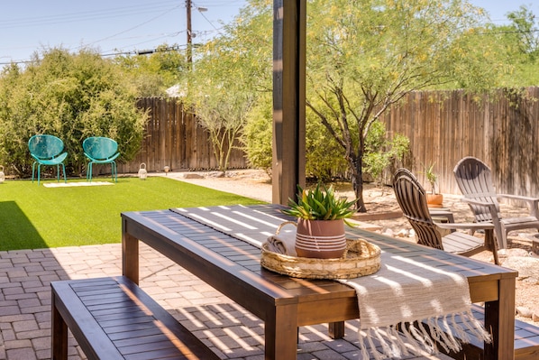 A patio with a wooden table, chairs, and a small garden area with a lawn and trees.