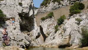 A rocky landscape with a small pool and two people sitting on the rocks.