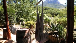 A hammock suspended from a wooden structure, a rustic barrel, and a view of a mountainous landscape.