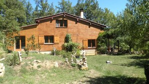 A wooden cabin with a sloped roof, a chimney, and a small porch with a bench.