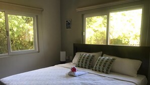 A neatly made bed with a white bedspread and two pillows, a small framed picture on the wall, and a window with a view of trees. - Amazing Heated Jacuzzi, Private Pool, 2 Bed/Bath, AC in Everyroom!!!! (Sosúa)