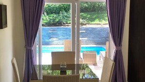 A room with a glass door leading to a pool area, wicker furniture, and purple curtains. - Amazing Heated Jacuzzi, Private Pool, 2 Bed/Bath, AC in Everyroom!!!! (Sosúa)