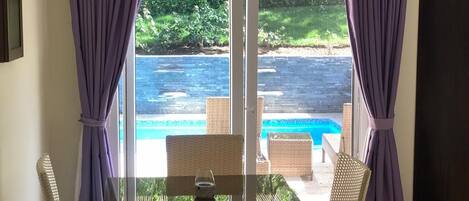 Una habitación con puerta de vidrio que da a una zona de piscina, muebles de mimbre y cortinas moradas.