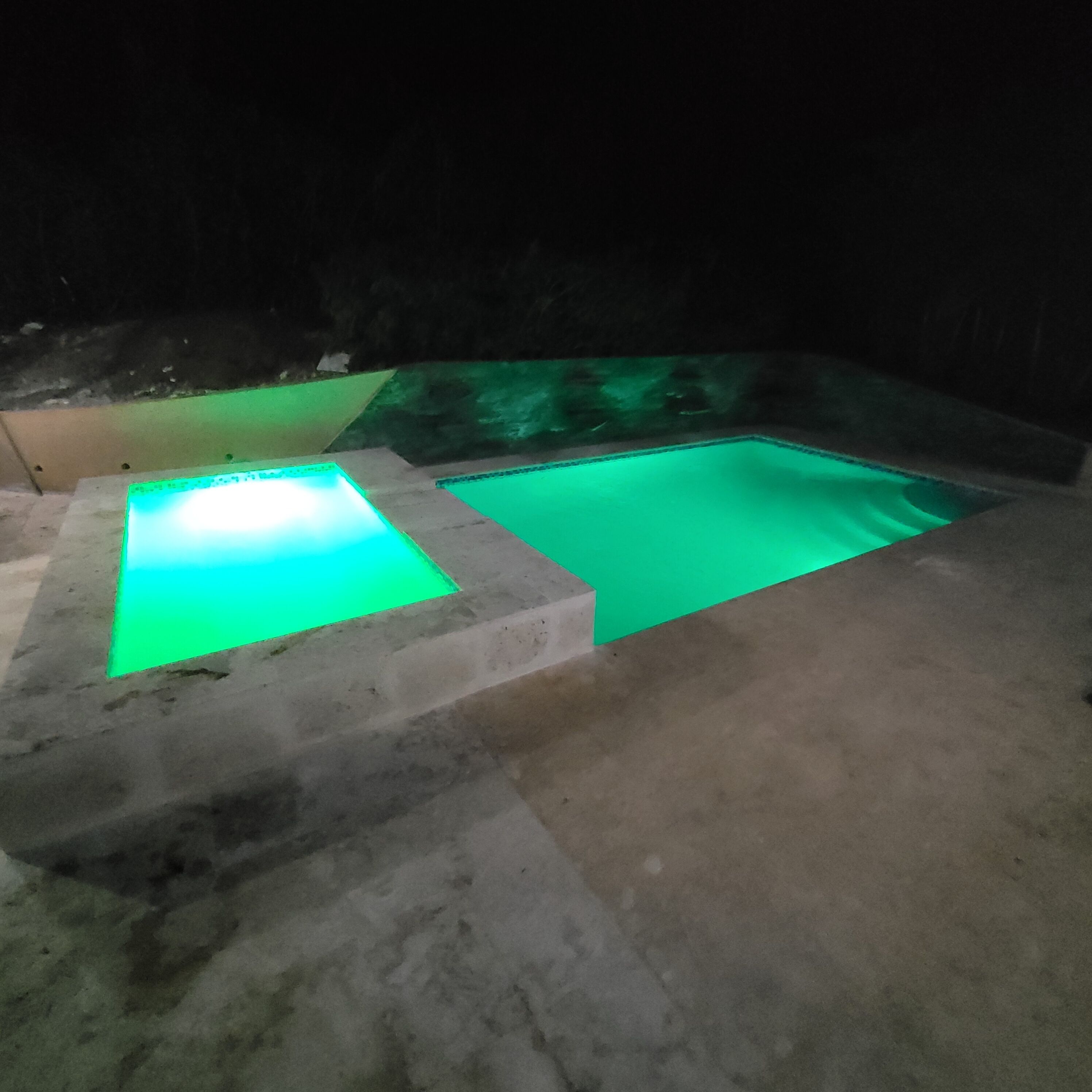 Una piscina con borde iluminado en verde y un suelo de hormigón.