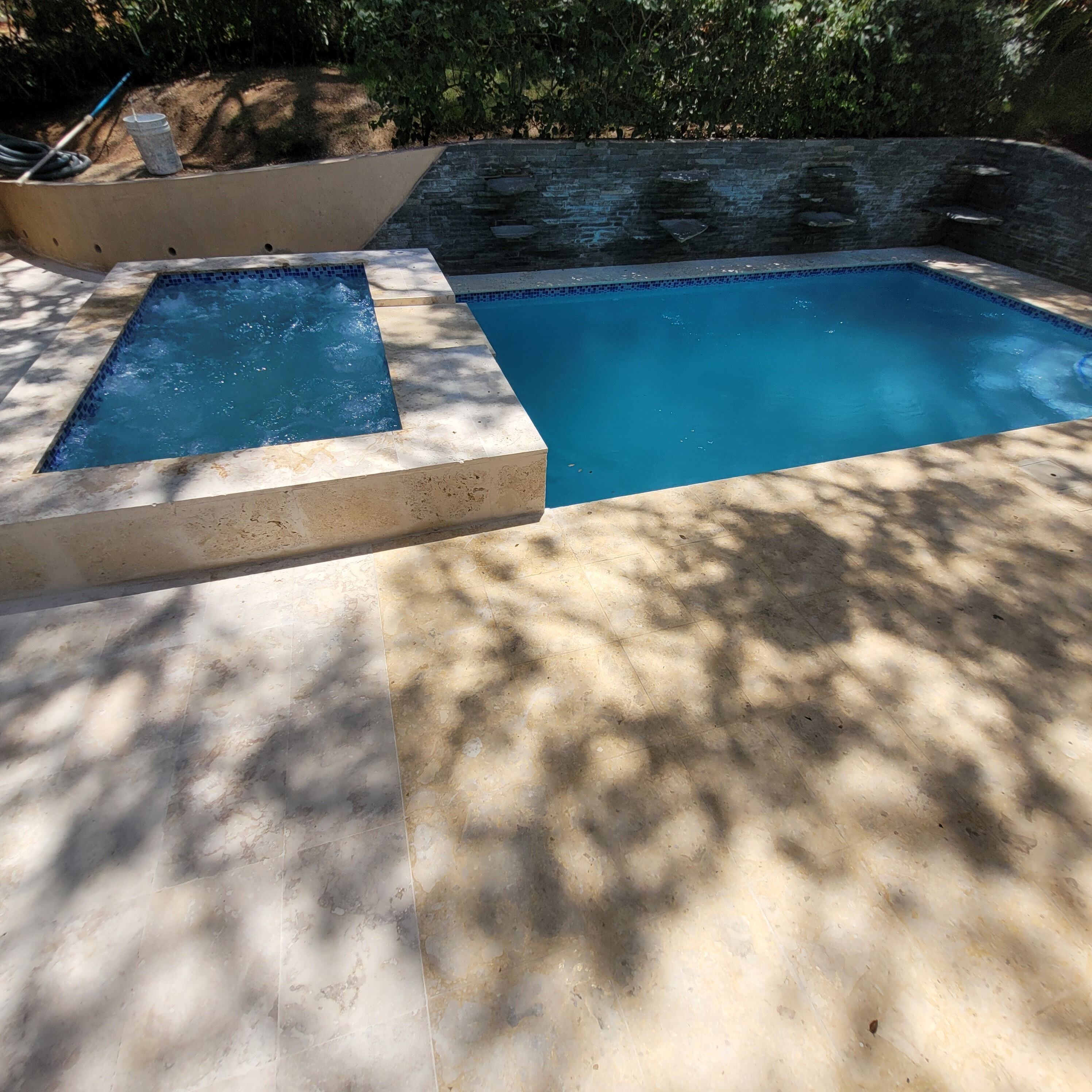 Una piscina rectangular con un muro de piedra al fondo.