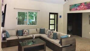 A modern living room with a sectional sofa, a glass coffee table, a ceiling fan, and a large window. - Amazing Heated Jacuzzi, Private Pool, 2 Bed/Bath, AC in Everyroom!!!! (Sosúa)