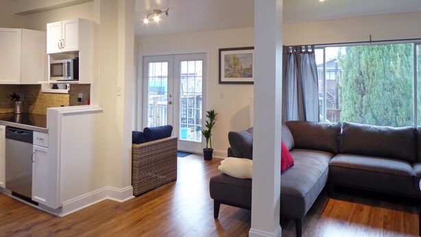 A spacious living area with a grey sofa, a dining table, and a kitchen area with white cabinets and a microwave. - 5-bedroom home perfect for families/ groups. Located just minutes DT Vancouver (Vancouver)