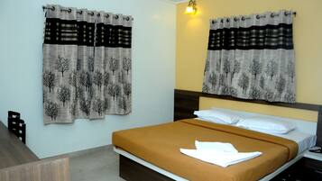 A hotel room with a bed, two curtains with tree patterns, a nightstand, and a wall-mounted light.